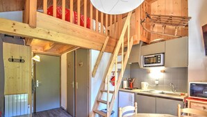 A cozy kitchen with wooden beams, a dining table, and a ladder leading to a loft bedroom. - Renovated studio by the cable car, parking, WiFi (Morzine)