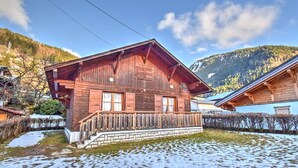 A wooden chalet with a balcony, surrounded by snow-covered ground and mountains in the background. - Unique chalet near Morzine center with private garden and WiFi, sleeps 5 (Morzine)