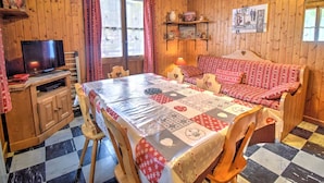 A cozy cabin interior with a wooden floor, a dining table with a quilt, a sofa, a television, and a fireplace. - Unique chalet near Morzine center with private garden and WiFi, sleeps 5 (Morzine)