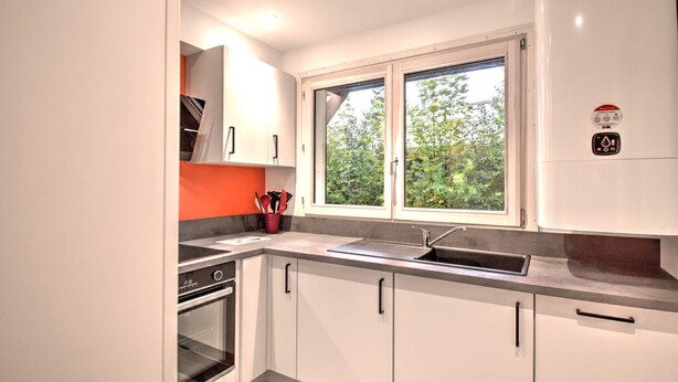A modern kitchen with white cabinets, a built-in oven, a window with a view of greenery, and a stainless steel sink. - Unique chalet near Morzine center with private garden and WiFi, sleeps 5 (Morzine)