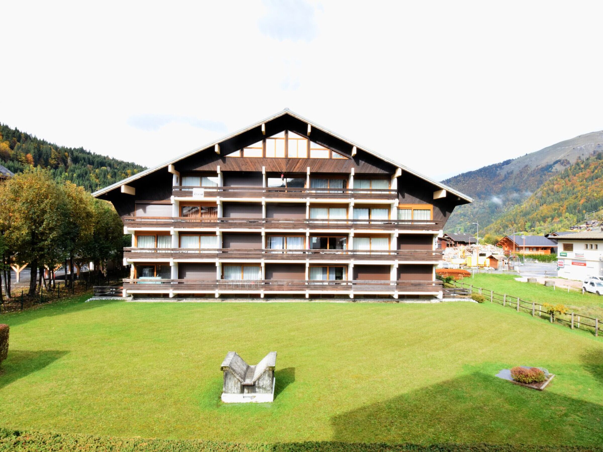 A multi-story hotel with a wooden facade and balconies, set against a mountainous backdrop.