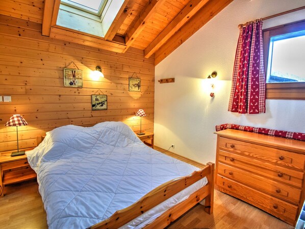 Un dormitorio de madera con cama, lámparas de noche, cómoda y luces fijadas a la pared.