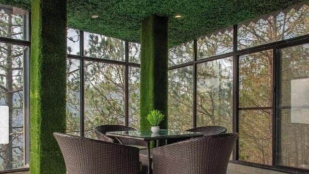 A dining area with wicker chairs and a glass table, surrounded by large windows with a view of trees. - JP Restaurant And Resort (Solan)