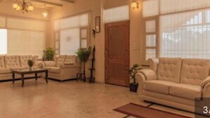 A spacious living room with a high ceiling, large windows, and a wooden door. - JP Restaurant And Resort (Solan)