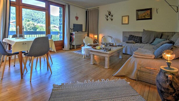 A cozy living room with a dining area, a sofa set, a television, and a view of the outdoors.