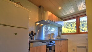 A modern kitchen with a built-in oven, a stainless steel range hood, and a window with a view of the outdoors.