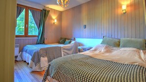 A cozy room with two beds, wooden walls, a large window with curtains, and a unique spherical light fixture.