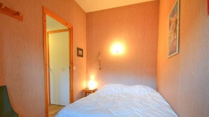 Ein Schlafzimmer mit einem Bett, einem Sessel, einem Nachttisch mit Lampe und einer Tür zu einem anderen Raum.