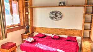 A bedroom with a wooden headboard, a red bedspread, and a wall-mounted clock. - Studio in central Morzine with balcony and WIFI (Morzine)