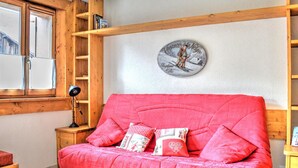 A cozy room with a red sofa, wooden shelves, a small table, and a wall-mounted picture. - Studio in central Morzine with balcony and WIFI (Morzine)
