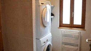 A laundry room with a stacked washer and dryer, a window with wooden shutters, and a white radiator. - Studio in central Morzine with balcony and WIFI (Morzine)