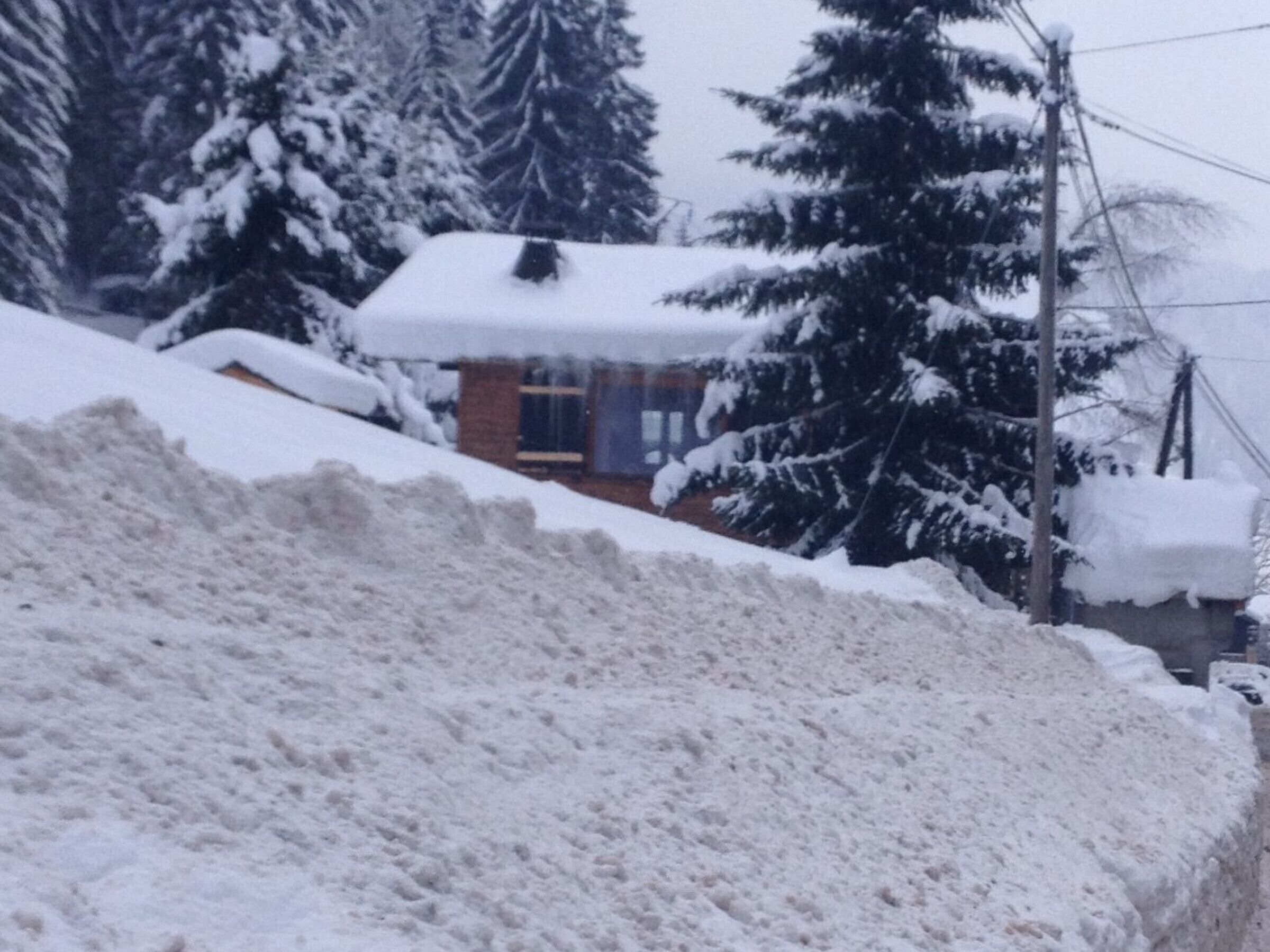 A snow-covered landscape with a pile of snow in the foreground and a building with a snow-covered roof in the background.