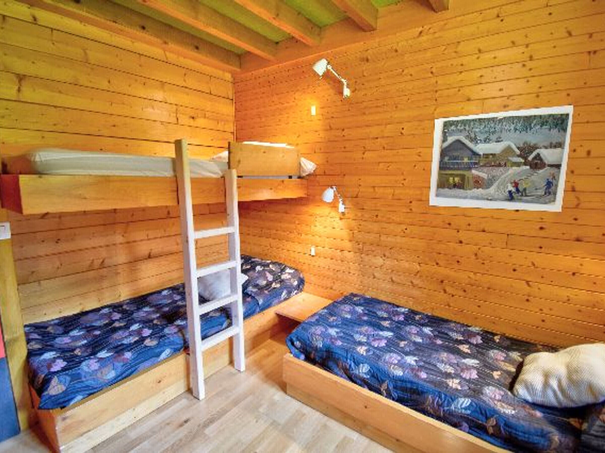 Een blokhut met twee stapelbedden, een ladder, een klein tafeltje en een lijst met een foto aan de muur.