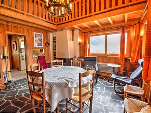Cozy room with a round table, wooden chairs, and a fireplace, offering a view of the outdoors.