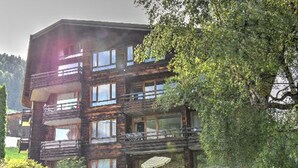 A multi-story wooden building with balconies, a gravel driveway, and lush greenery. - Studio with southwest-facing balcony, parking, pets allowed, 300m from center (Morzine)