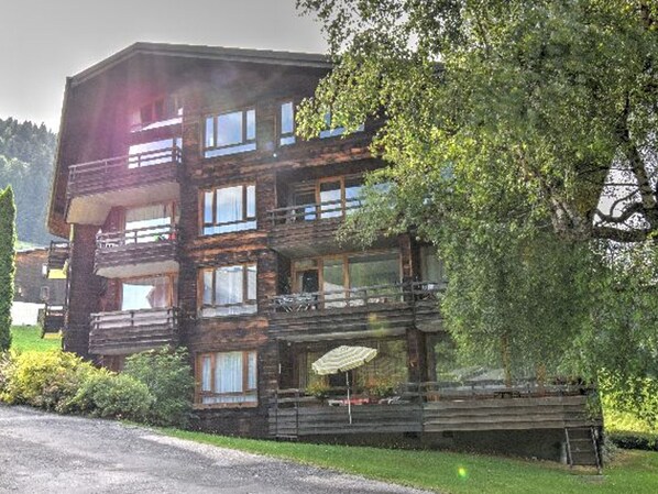 A multi-story wooden building with balconies, a gravel driveway, and lush greenery. - Studio with southwest-facing balcony, parking, pets allowed, 300m from center (Morzine)