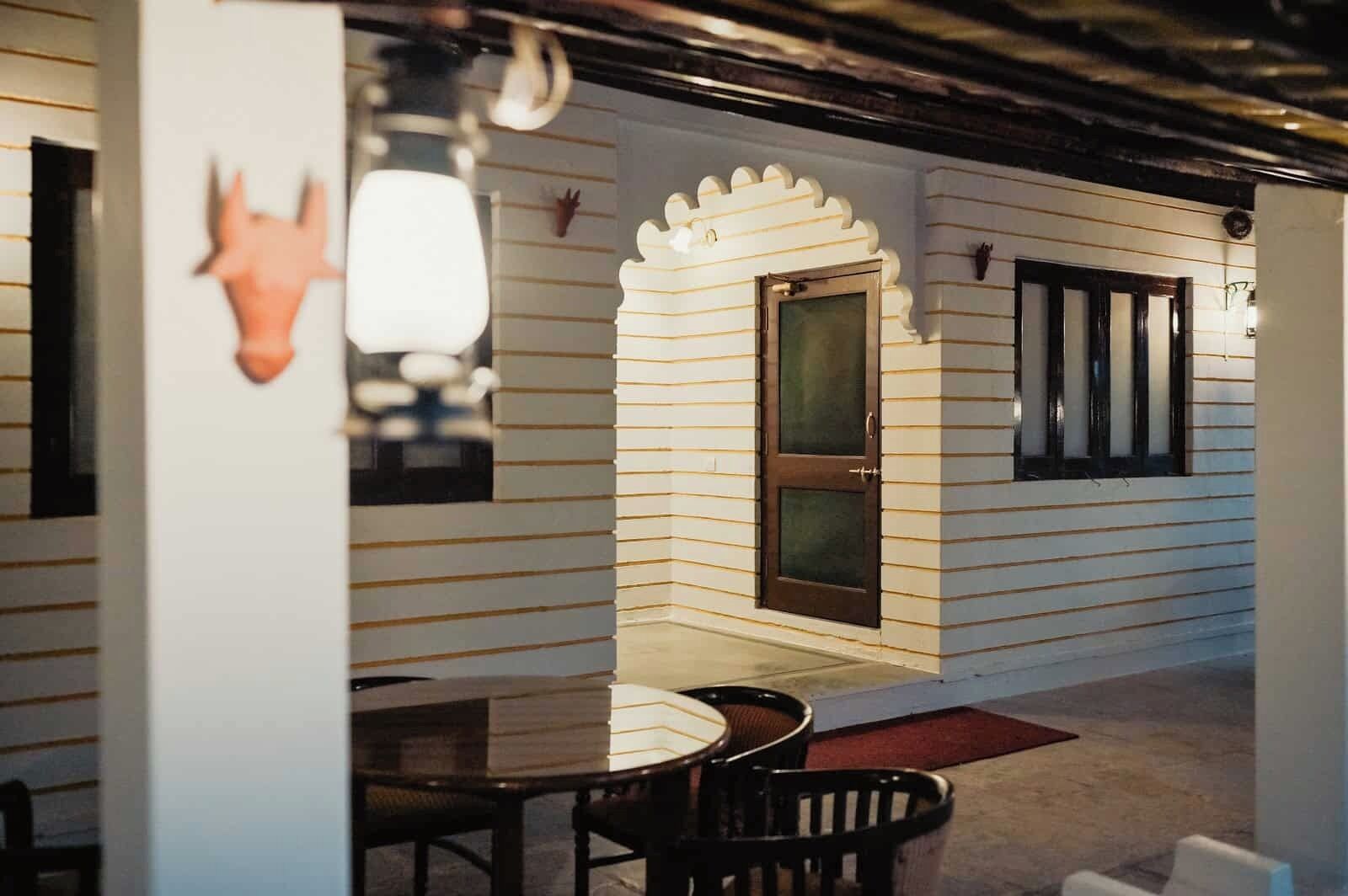 A covered outdoor seating area with a table and chairs, a door, and a window.