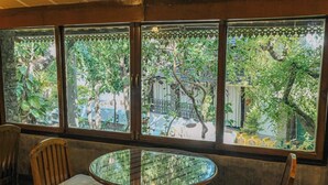 Ein Zimmer mit einem runden Glastisch und zwei Holzsesseln, ein großes Fenster mit Blick auf einen Garten und ein Gebäude draußen.