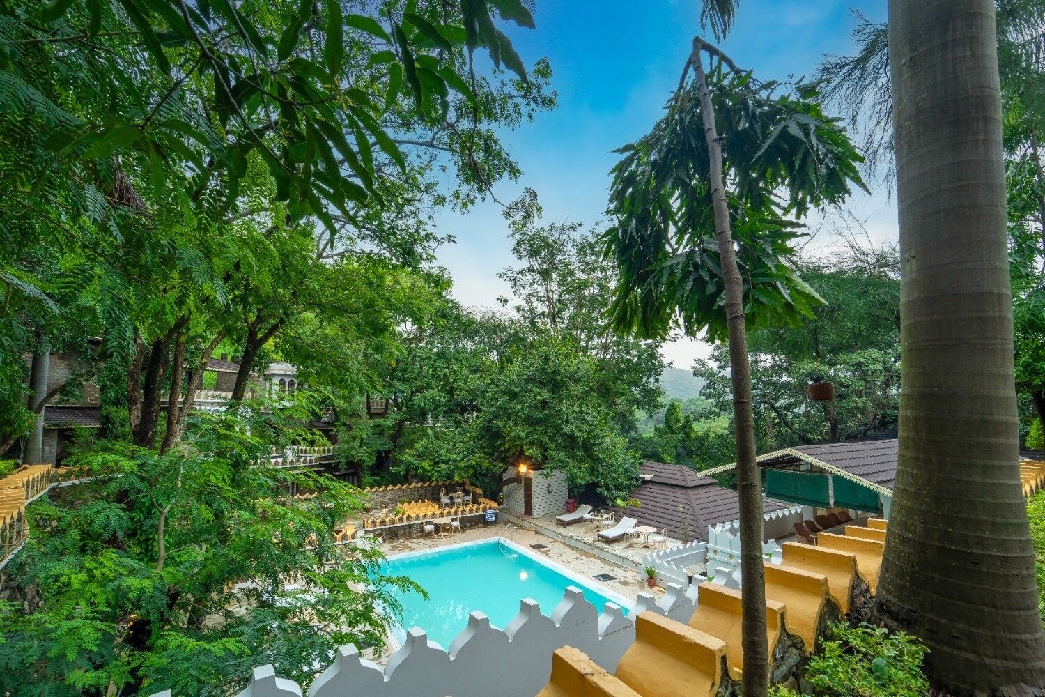 Una piscina rodeada de abundante vegetación y arquitectura tradicional.