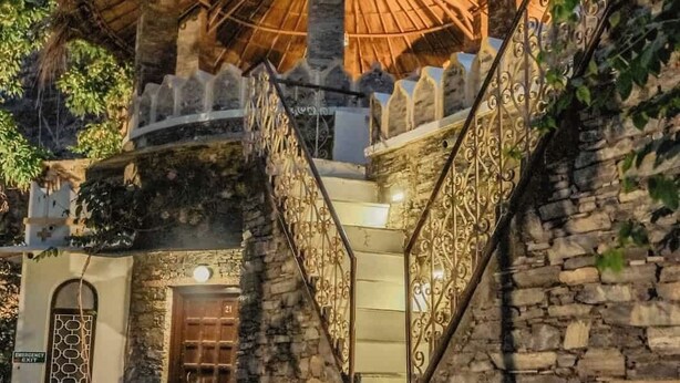 Eine Treppe führt zu einem Gebäude mit einem Strohdach, Steinmauern und schmiedeeisernen Geländern.