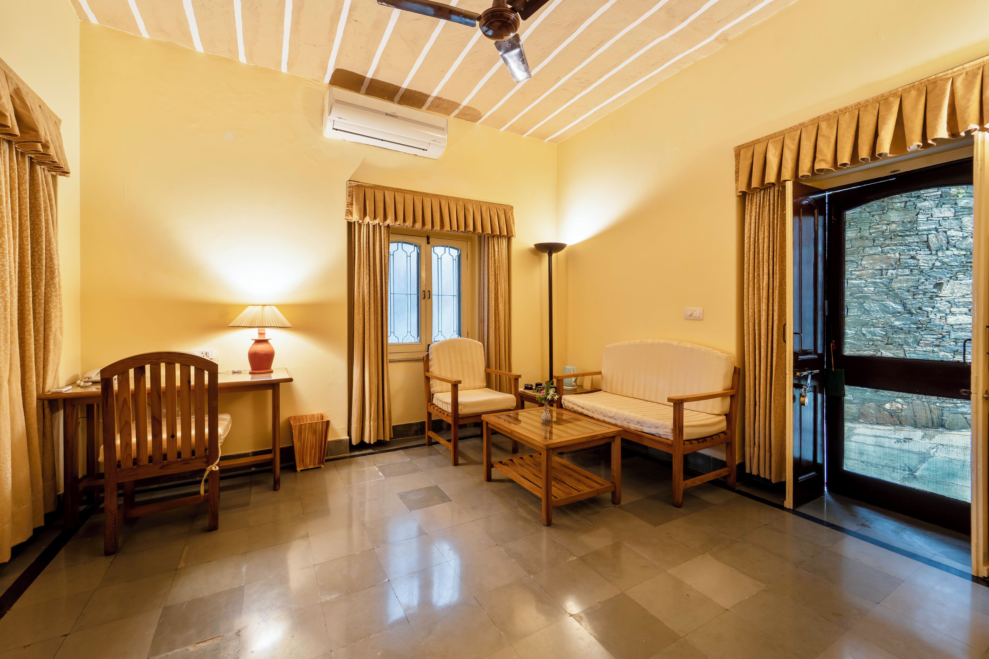 A room with a ceiling fan, an air conditioning unit, a sofa, a chair, a small table, and a window with curtains.