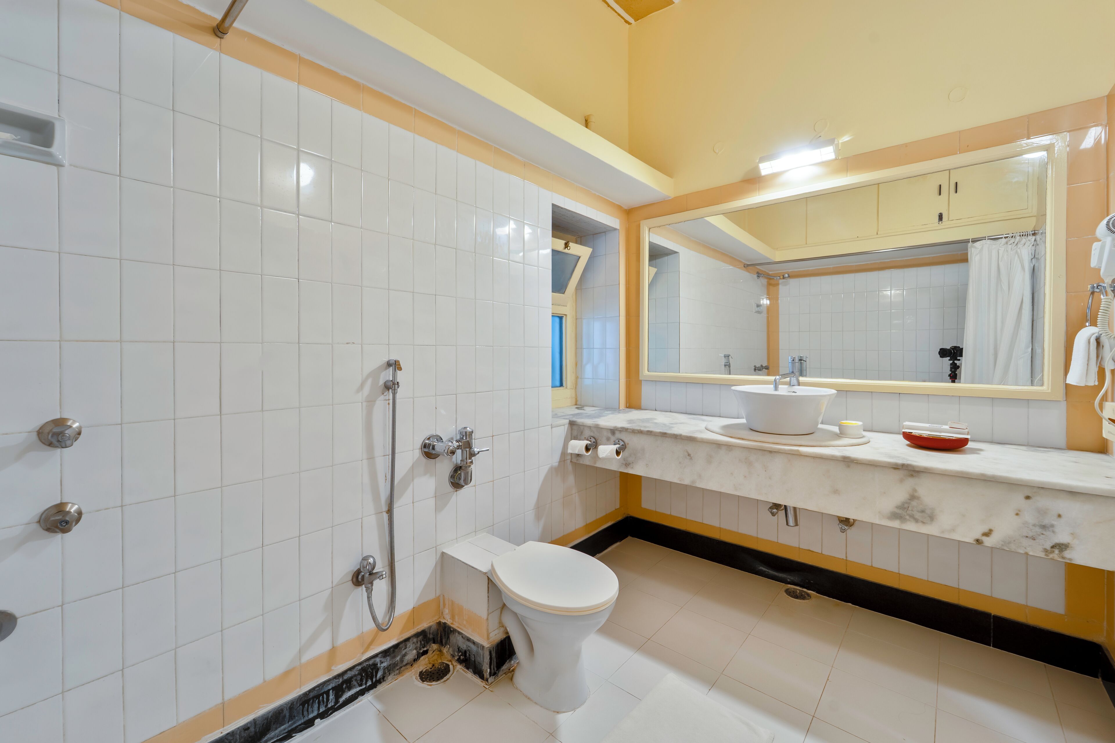 A bathroom with white tiled walls, a white toilet, a sink with a mirror above it, and a shower area.