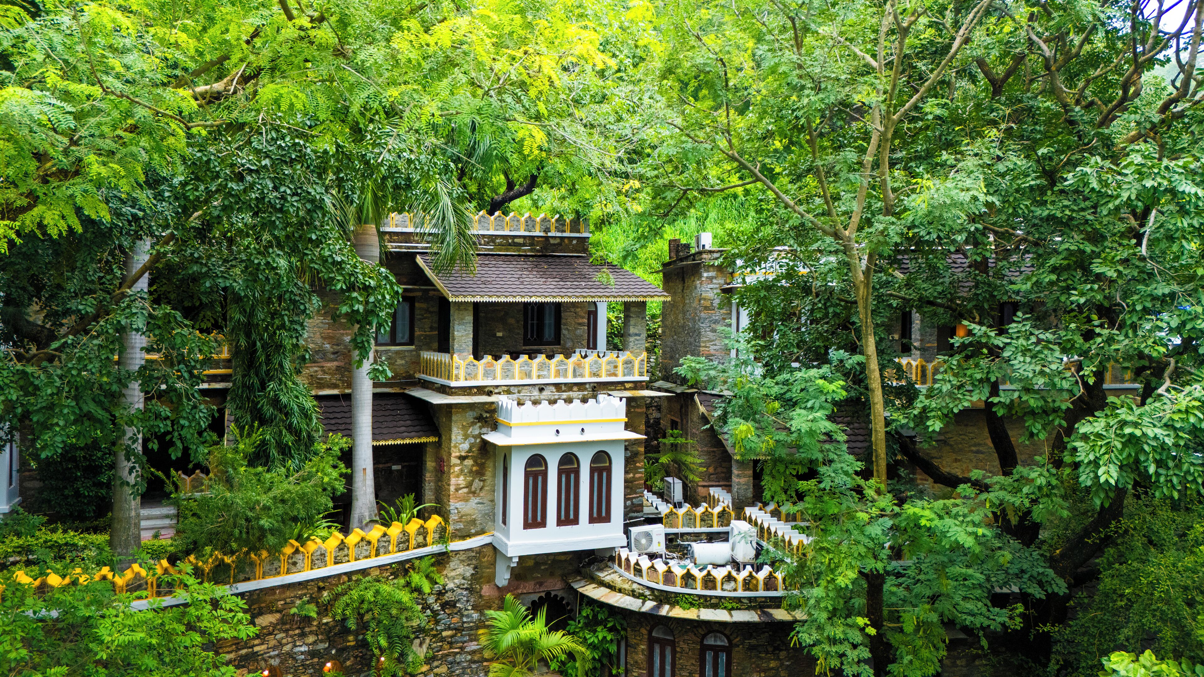A multi-level stone building with balconies, surrounded by dense greenery.