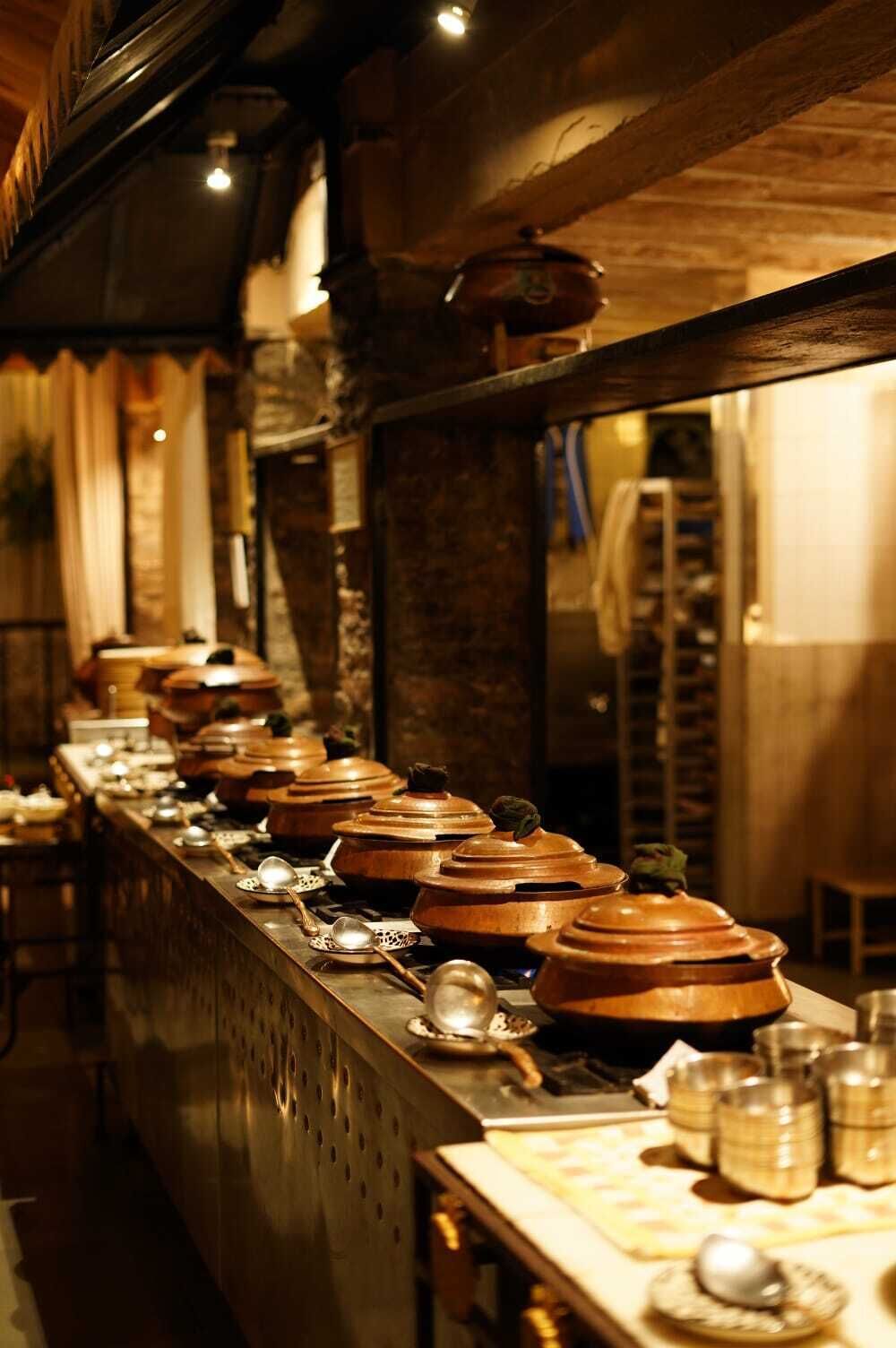 Un long comptoir orné de nombreux pots en argile et d’ustensiles de cuisine, ce qui laisse supposer qu’il s’agit d’une cuisine ou d’un coin repas.