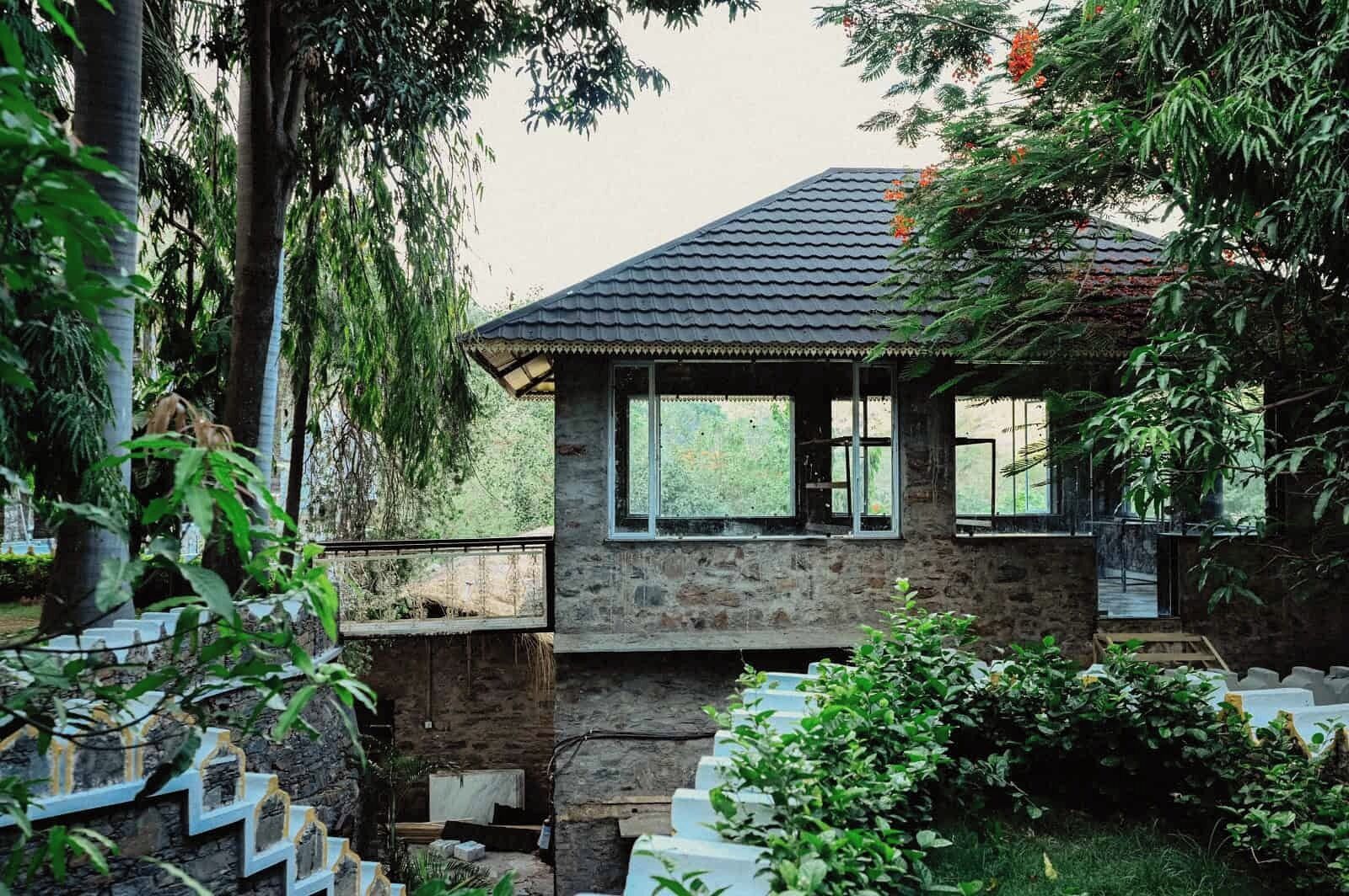 Una casa de piedra con techo de tejas, rodeada de abundante vegetación y una escalera que lleva a un balcón.