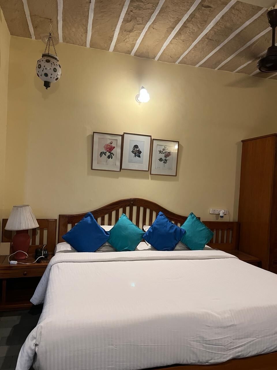 A bedroom with a wooden bed, a nightstand with a lamp, and wall-mounted artwork.
