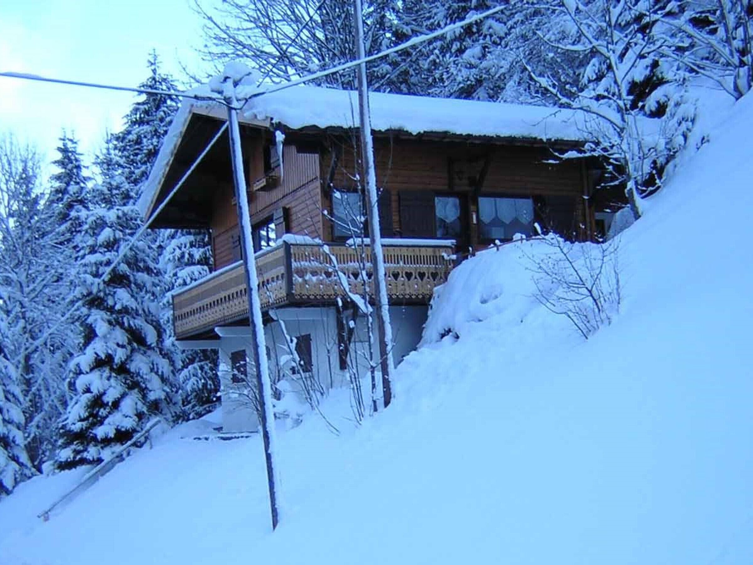 A wooden cabin with a balcony, surrounded by snow-covered trees.
