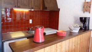 Eine Küche mit Holzausstattung, einer roten Fliesenrückwand und einer Kaffeemaschine auf der Arbeitsfläche.