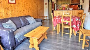 Ein gemütliches Wohnzimmer mit einem dunkelgrauen Sofa, einem Holztisch und einem Essbereich mit roter Tischdecke.