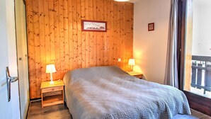 Ein Schlafzimmer mit einer Holzwand, einem Bett mit grauer Decke, zwei Nachttischlampen und einem Bilderrahmen.