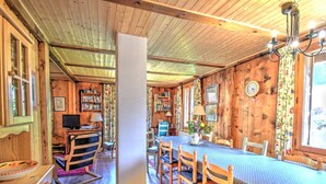 Ein gemütliches Blockhaus-Interieur mit Esstisch, Stühlen, Bücherregal und Fernseher.