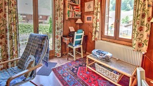 Ein gemütliches Zimmer mit Holzvertäfelung, einem Schaukelstuhl, einem Schreibtisch mit Stuhl, einem Bücherregal und einem Fenster mit Vorhängen.