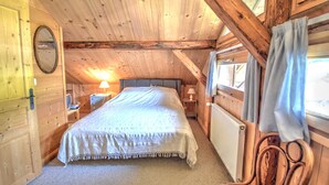 Ein gemütliches Schlafzimmer einer Holzjagdhütte mit einem Bett, einem Nachttisch, einer Lampe und einem Sessel.