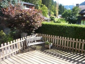 A wooden deck with a bench and a potted plant, surrounded by a wooden fence and lush greenery.
