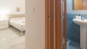 Ein Schlafzimmer mit einem Bett, einem Nachttisch und einem Badezimmer mit Waschbecken und Spiegel.