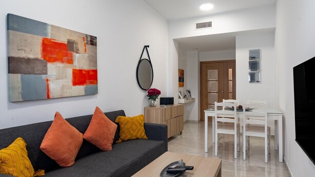 Ein modernes Wohnzimmer mit grauem Sofa, Holz-Couchtisch und einem Essbereich mit weißen Stühlen und einem Tisch.