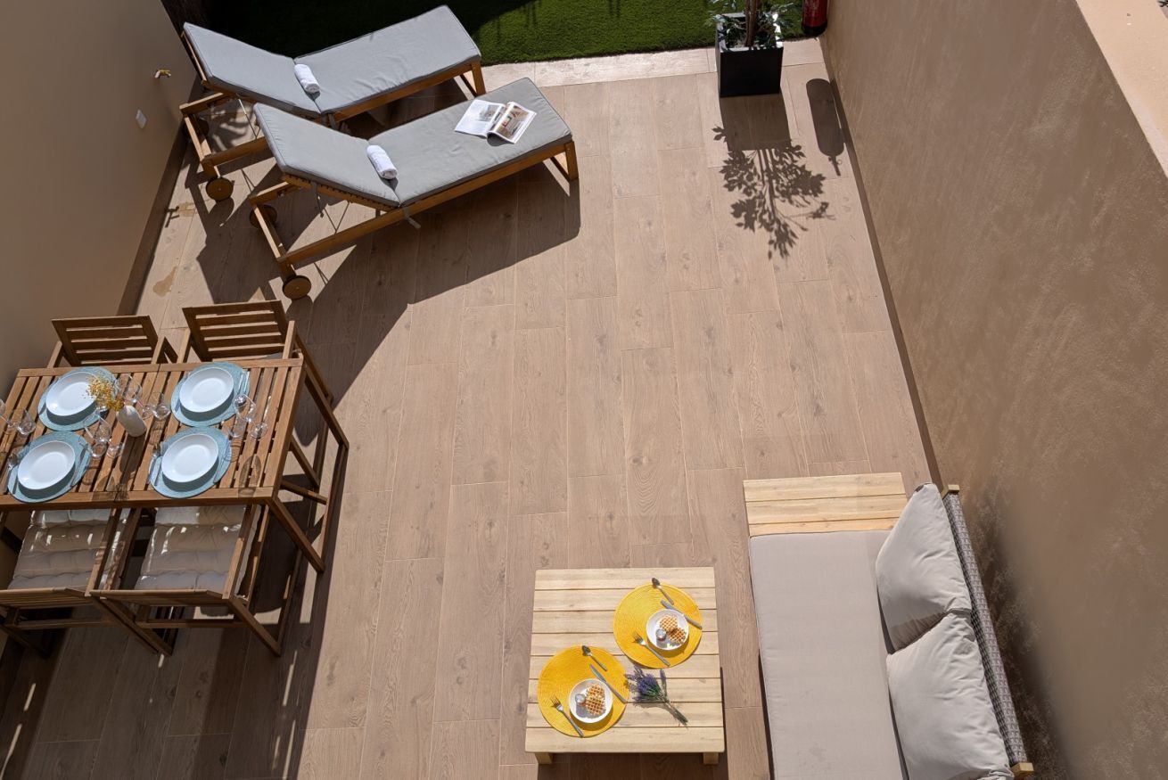 A rooftop terrace with a dining table set for four, a lounge area with two chairs, and a small table with two yellow lamps.