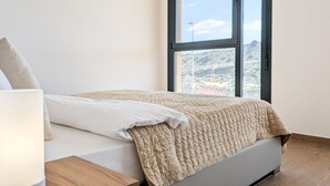 Un dormitorio con cama, mesita de noche y ventana con vista a un paisaje montañoso.