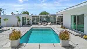 A modern house with a rectangular swimming pool, outdoor seating area, and palm trees.
