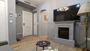 Een woonkamer met een open haard, een flatscreen-tv, een bank en een salontafel met tijdschriften en glazen.