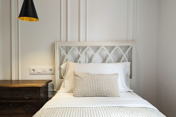 A neatly made bed with white bedding and a textured pillow, a wooden nightstand with drawers, and a pendant light fixture.