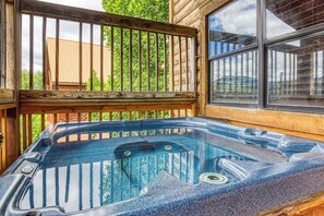 Relax in the hot tub on the deck, surrounded by lush greenery and a large window.