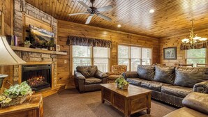 A cozy log cabin interior with a fireplace, leather furniture, and a ceiling fan. - It's 5 O'clock Somewhere: Hot Tub, Theater Room, Free Tickets, Game Room!!! (Gatlinburg)