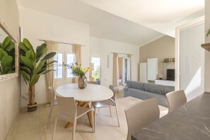 Een moderne woonkamer met een ronde eettafel, een grijze bank en een grote potplant.
