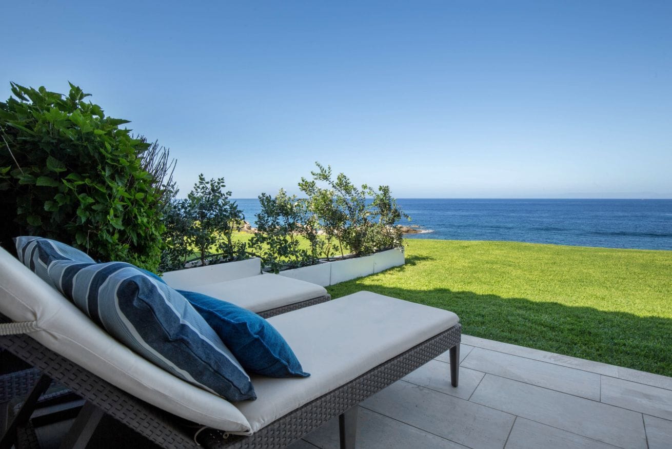Eine Terrasse mit zwei Lounge-Stühlen, einer Rasenfläche und Blick auf das Meer.