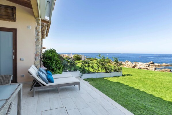 A patio with a view of the sea, a lounge chair, and a small table.
